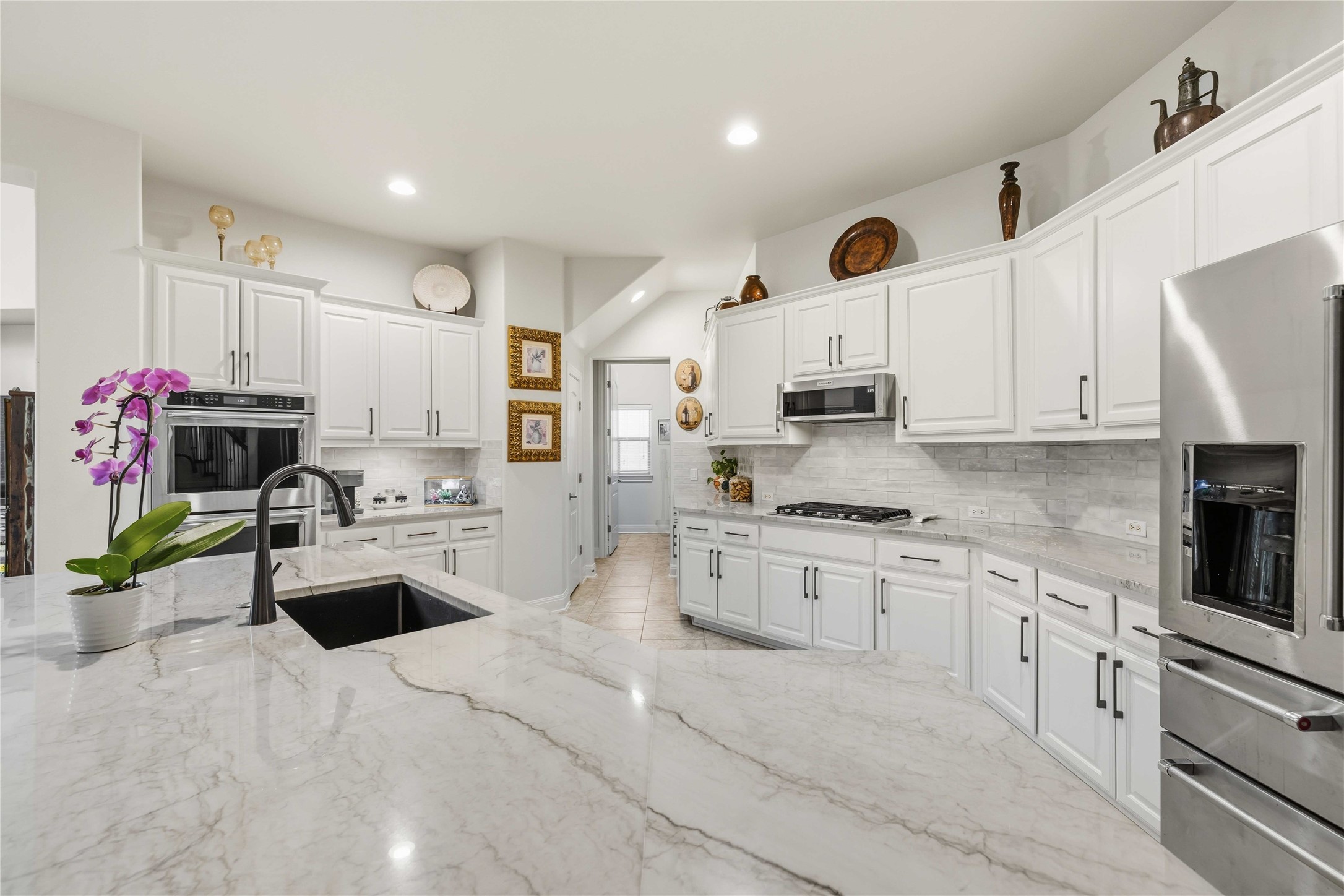 15200 Spillman Ranch Loop Austin, TX 78738 - Photo 12 of 40 The kitchen features white cabinetry, a large kitchen island with a dark sink and matte black faucet, stainless steel appliances, and a tiled backsplash