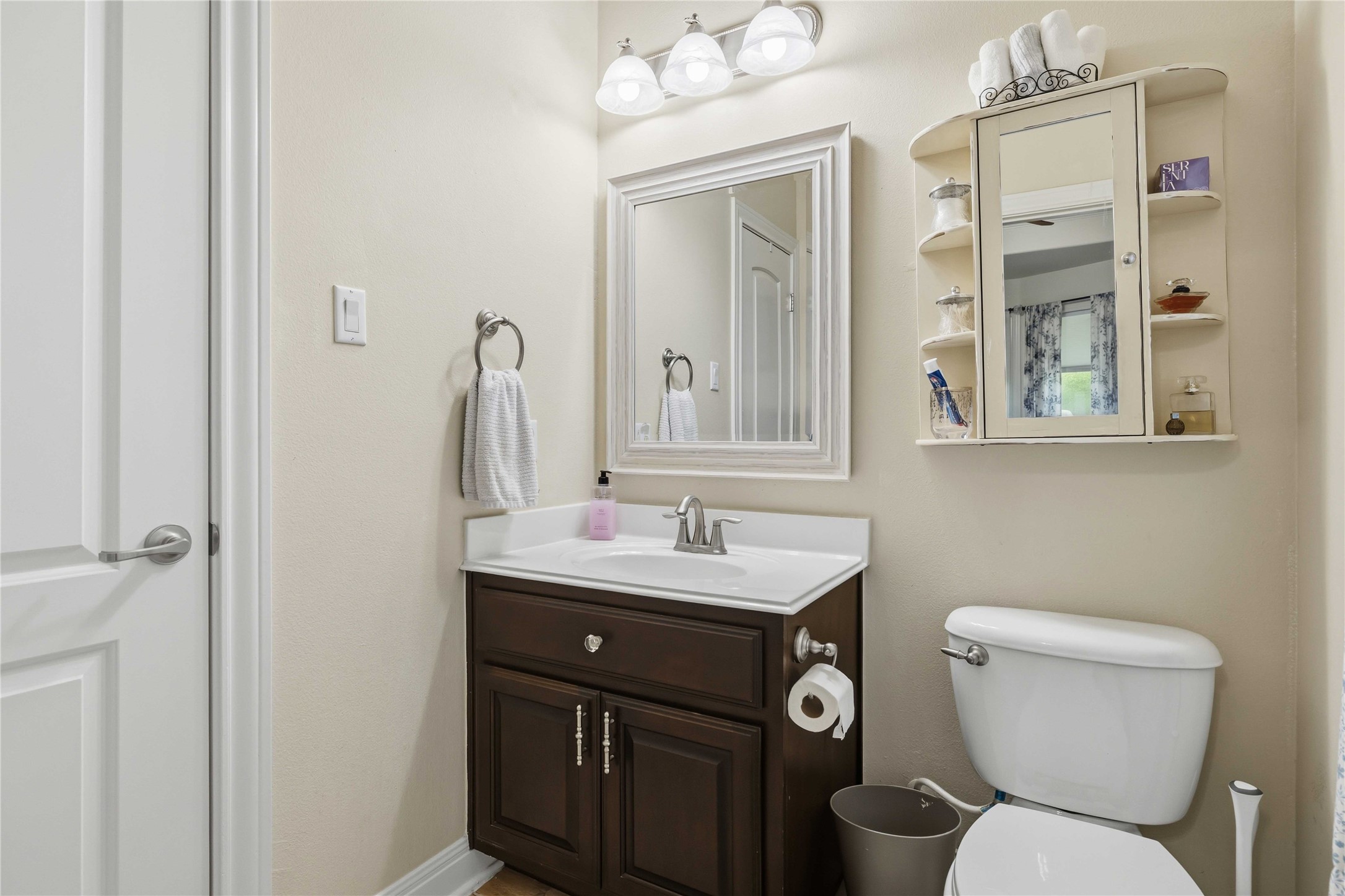 15200 Spillman Ranch Loop Austin, TX 78738 - Photo 30 of 40 The bathroom features a dark wood vanity with a white countertop and an integrated sink, a rectangular framed mirror, and a wall-mounted medicine cabinet with open shelving