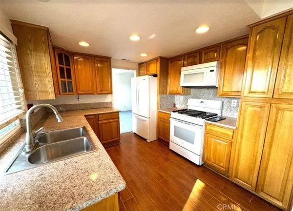 a kitchen with stainless steel appliances granite countertop a refrigerator a stove top oven a sink dishwasher and white cabinets with wooden floor