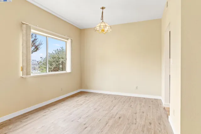 an empty room with wooden floor chandelier and windows