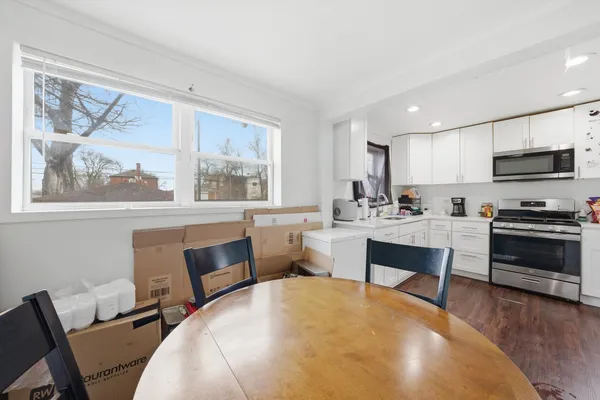 a living room with stainless steel appliances a dining table wooden floor and a large window