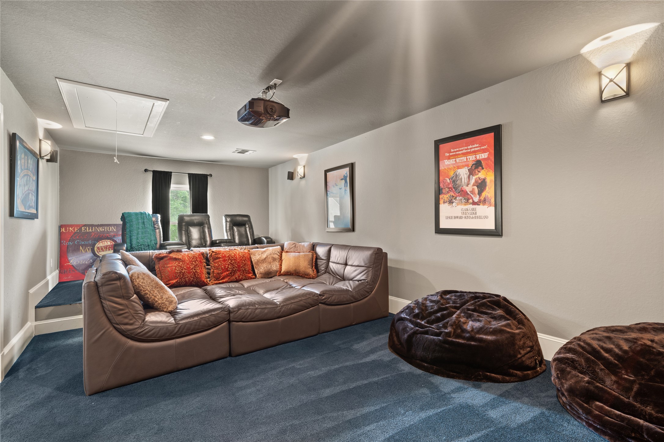 36 Wind River Drive Conroe, TX 77384 - Photo 40 of 45 This room features a cozy home theater setup with a large sectional sofa, plush bean bags, and a ceiling-mounted projector which all media equipment stays with the home. The walls are decorated with vintage movie posters, and there's a raised platform with additional seating. The space is carpeted and has soft lighting, creating an inviting atmosphere for movie nights.