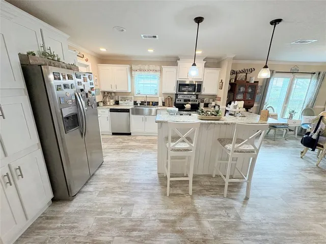 a kitchen with stainless steel appliances kitchen island granite countertop a refrigerator a stove a microwave oven a sink with island chairs and wooden floor