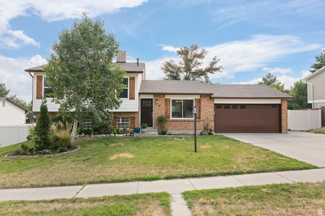 Split-level residence featuring a brick and white siding exterior, dark trim, and a brown garage door