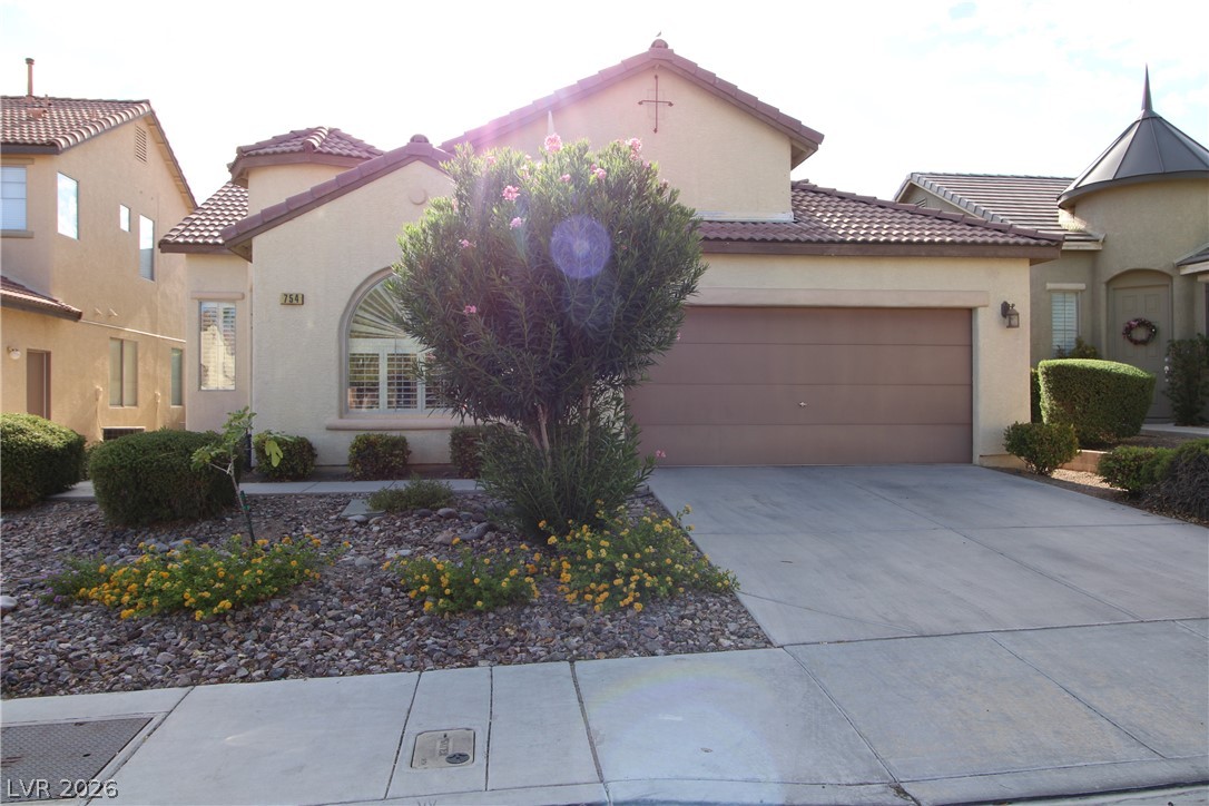 754 Rise Canyon Drive Henderson, NV 89052 - Photo 2 of 34 A well-maintained stucco home with a tile roof and attached garage, complemented by mature desert landscaping.