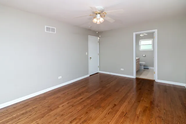 a view of an empty room with wooden floor and a ceiling fan