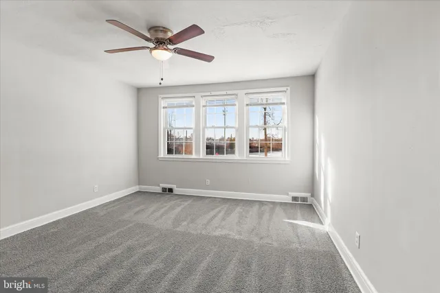 an empty room with chandelier fan and windows