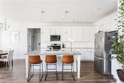 a kitchen with stainless steel appliances a refrigerator a stove a dining table and chairs with wooden floor