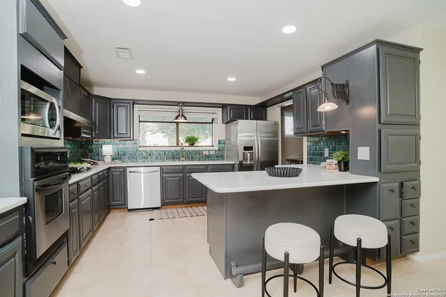 a kitchen with stainless steel appliances granite countertop a sink a stove a refrigerator cabinets and chairs