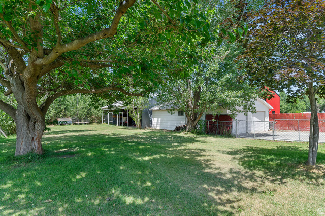 1489 North 400 West Bountiful, UT 84010 - Photo 37 of 47 Expansive grassy yard featuring mature trees, a detached garage with a white exterior, and a chain-link fence