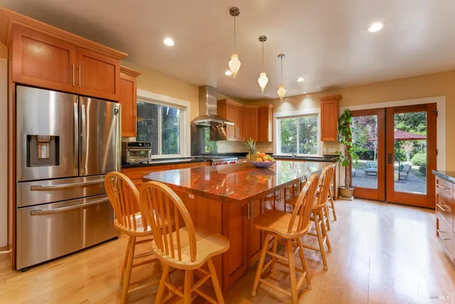 a kitchen with stainless steel appliances granite countertop a refrigerator a sink dishwasher a dining table and chairs with wooden floor