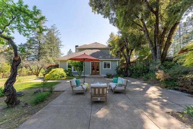 a view of a patio with table and chairs under an umbrella with large trees