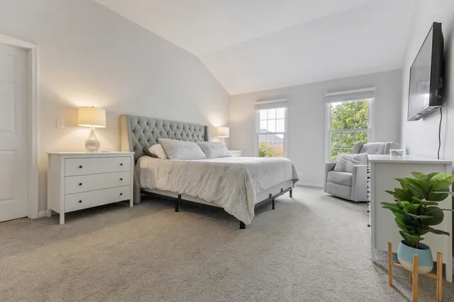 a spacious bedroom with a bed and a flat tv screen on dresser