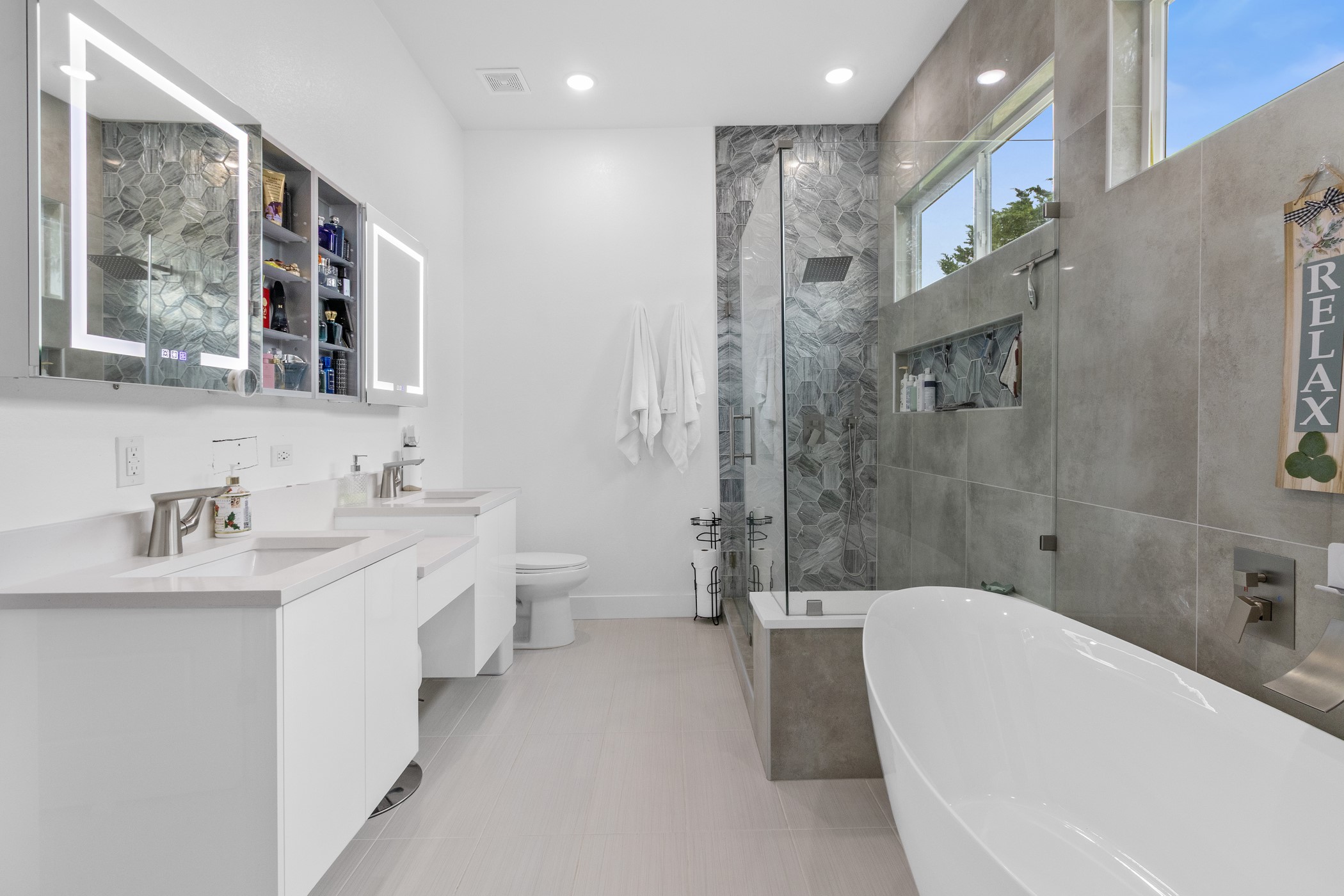 123 Zacate Street Elgin, TX 78621 - Photo 12 of 33 Contemporary bathroom featuring a freestanding soaking tub, a separate glass-enclosed shower with a tiled surround, and dual vanity sinks with quartz countertops