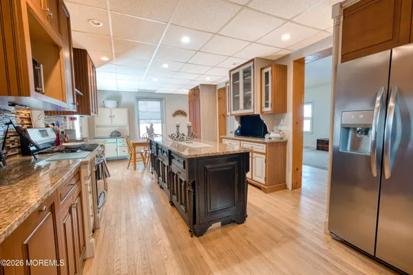 a kitchen with stainless steel appliances granite countertop a refrigerator a sink dishwasher a stove and a dining table with wooden floor