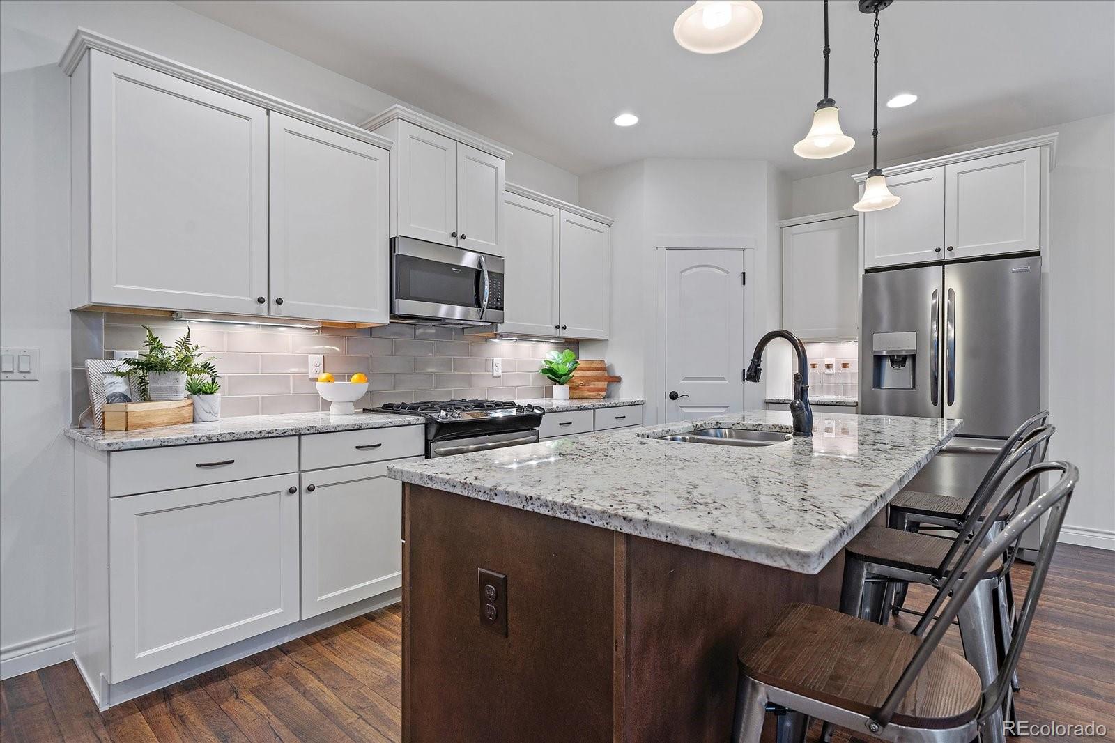 11526 Colony Loop Parker, CO 80138 - Photo 14 of 29 a kitchen with stainless steel appliances granite countertop a sink a stove a refrigerator and island with wooden floor