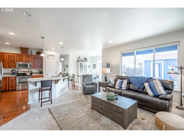 a living room with stainless steel appliances kitchen island granite countertop a table chairs and a refrigerator