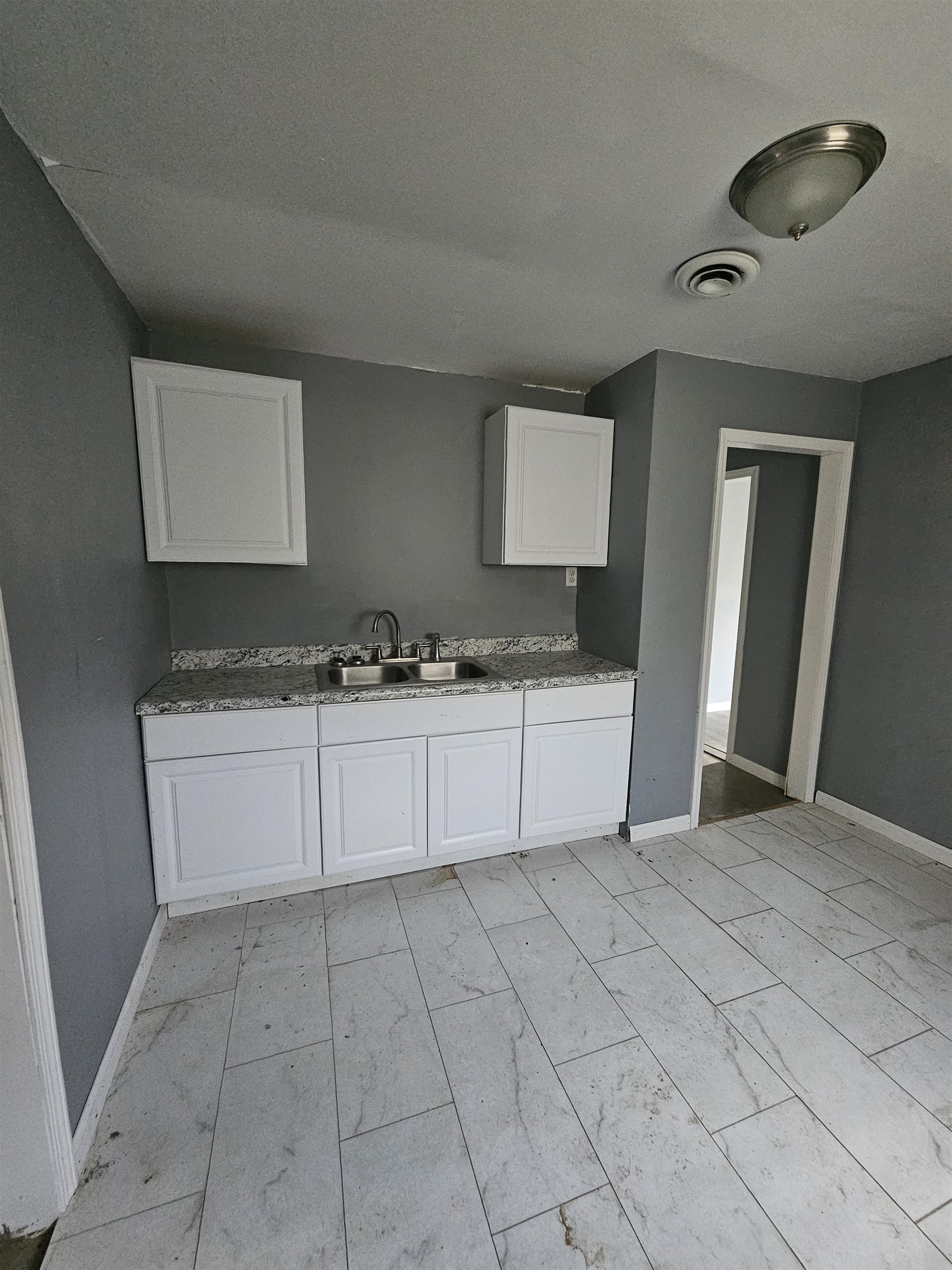 2059 Swift Street Memphis, TN 38109 - Photo 6 of 12 Kitchenette featuring light gray tile flooring, white shaker-style cabinetry, and a double basin stainless steel sink with a speckled countertop