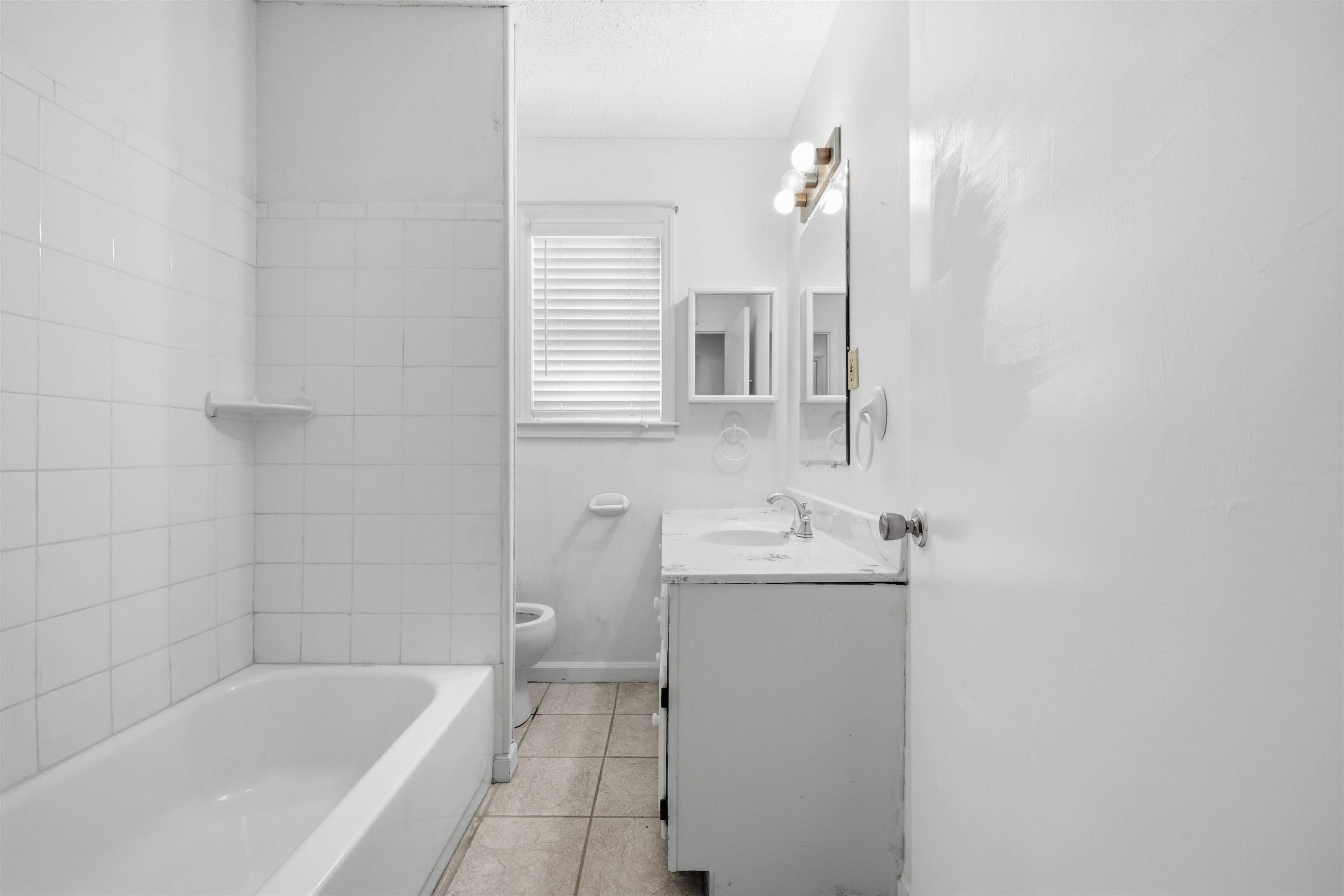 3007 Ruskin Road Bartlett, TN 38134 - Photo 23 of 37 Bathroom featuring a white bathtub, ceramic tile surround, window with blinds, vanity with integrated sink, and wall-mounted mirror