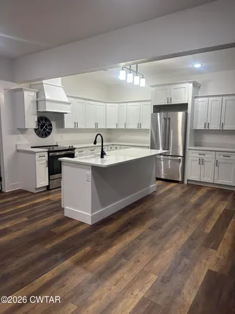 a kitchen with stainless steel appliances granite countertop a sink a stove a refrigerator and white cabinets