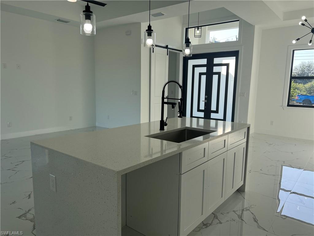 3510 15th Street Southwest Lehigh Acres, FL 33976 - Photo 23 of 50 Kitchen featuring a center island with sink, hanging light fixtures, a barn door, light stone countertops, and white cabinetry