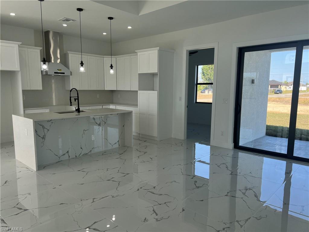3510 15th Street Southwest Lehigh Acres, FL 33976 - Photo 26 of 50 Kitchen featuring light stone counters, wall chimney exhaust hood, a kitchen island with sink, sink, and white cabinetry