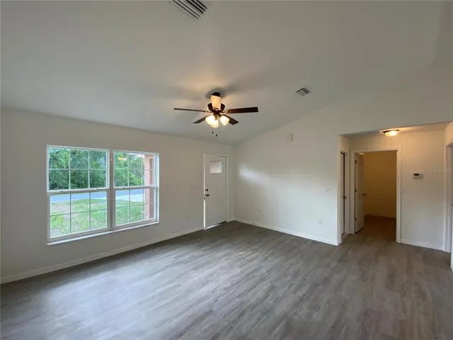 an empty room with wooden floor chandelier fan and windows
