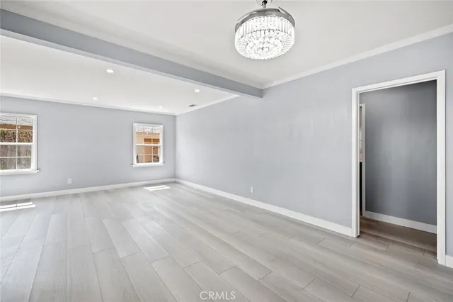 an empty room with wooden floor chandelier and windows