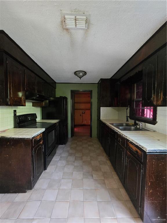 519 East 3rd Street Sullivan City, TX 78595 - Photo 7 of 12 Kitchen featuring backsplash, tile counters, range, a textured ceiling, and dark brown cabinetry