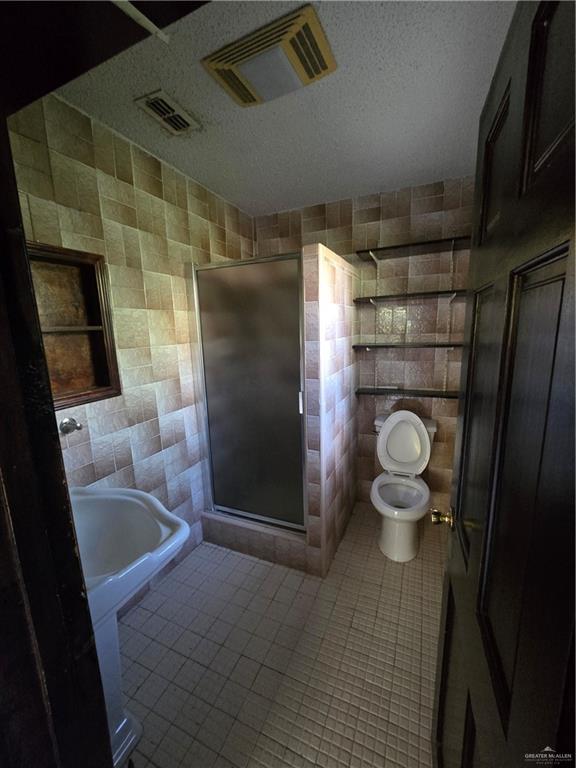 519 East 3rd Street Sullivan City, TX 78595 - Photo 9 of 12 Bathroom with tile walls, a stall shower, tile patterned flooring, and a textured ceiling