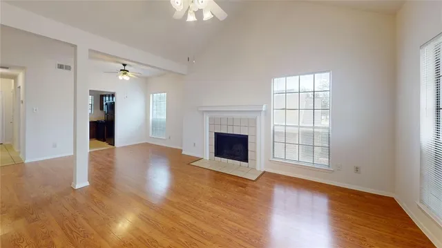 an empty room with wooden floor fireplace and windows