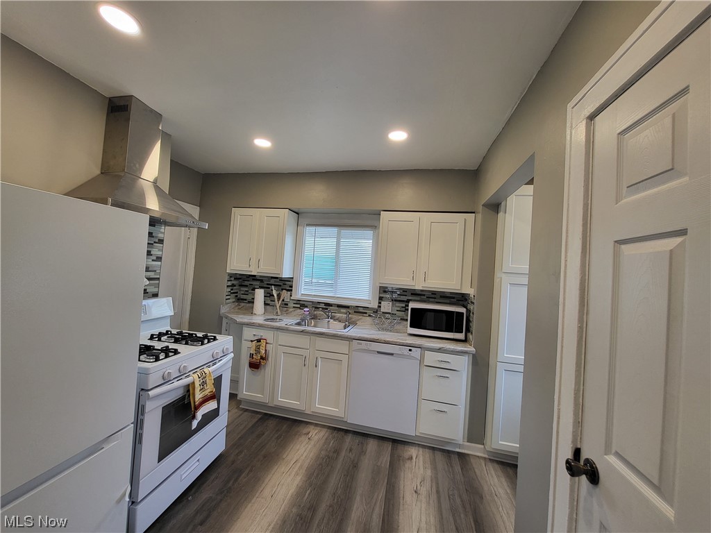 955 Nela View Road Cleveland Heights, OH 44112 - Photo 16 of 34 Kitchen featuring wall chimney range hood, white cabinets, white appliances, backsplash, and dark wood-type flooring