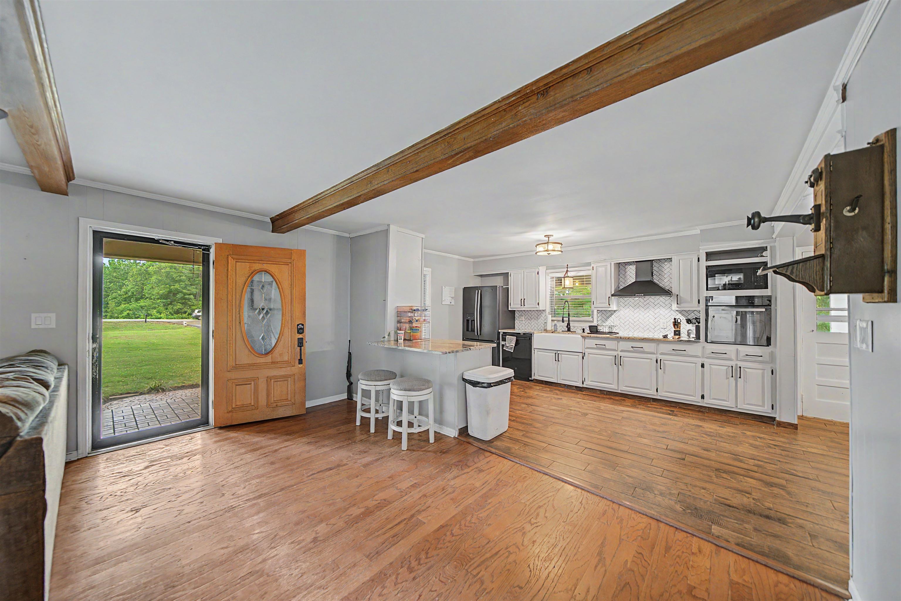 336 57th Highway West Ramer, TN 38367 - Photo 10 of 39 Open-concept kitchen and living area featuring wood-finish flooring, exposed ceiling beams, white cabinetry, a kitchen island with seating, and a farmhouse sink