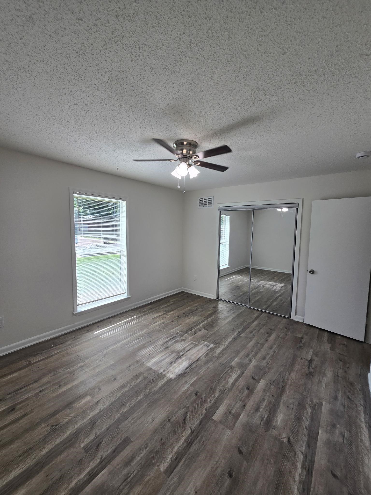 2889 Randy Cove Memphis, TN 38118 - Photo 13 of 18 Spacious room featuring wood-finish flooring, a window with white trim, a ceiling fan with light fixture, mirrored closet doors, and neutral wall paint