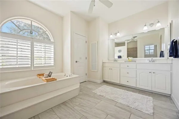 a spacious bathroom with a double vanity sink a mirror a bathtub and next to a window