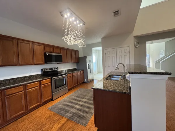 a kitchen with granite countertop stainless steel appliances a sink dishwasher a stove top oven a refrigerator with wooden floors