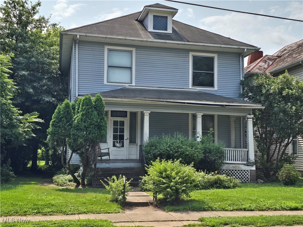 American foursquare style home with a porch, a front lawn, and a shingled roof