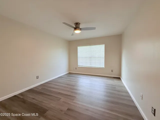 an empty room with wooden floor ceiling fan and window