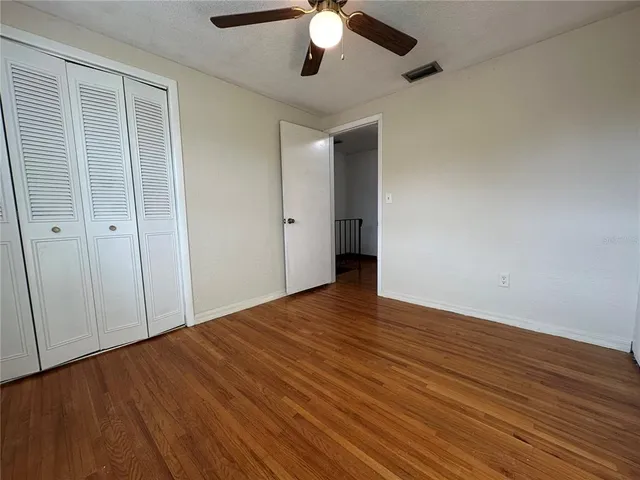 an empty room with wooden floor fan and windows