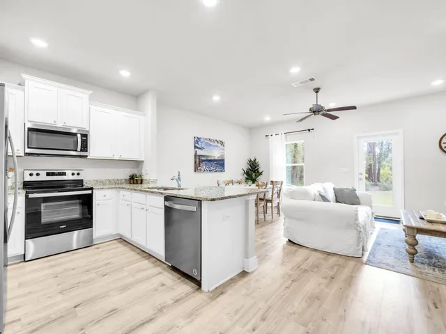 a kitchen with stainless steel appliances granite countertop a stove top oven a sink dishwasher and a refrigerator with wooden floor