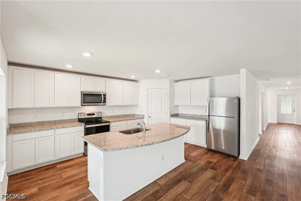 a kitchen with stainless steel appliances granite countertop a refrigerator a stove a sink and white cabinets with wooden floor