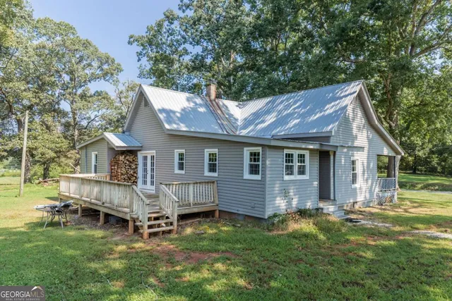 a house that is sitting in the grass with large trees and plants