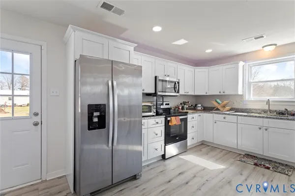 a kitchen with stainless steel appliances granite countertop a refrigerator a sink dishwasher a stove and white countertops with wooden floor