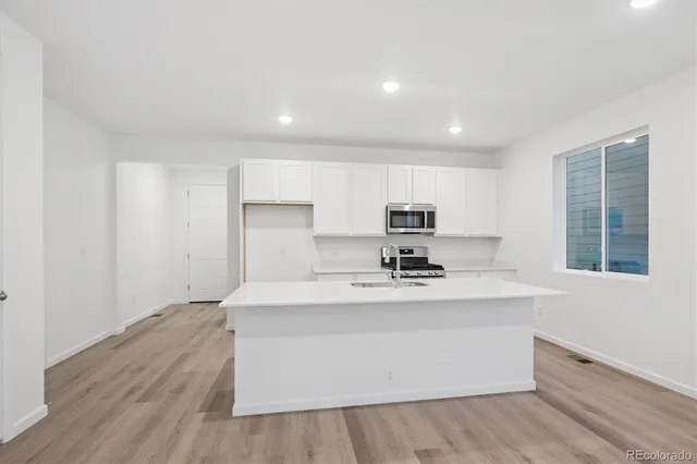 a large white kitchen with kitchen island a sink wooden floor and a refrigerator
