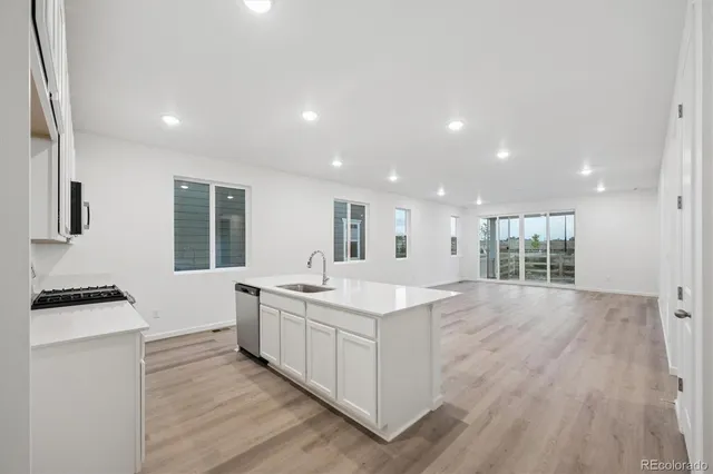 a kitchen with a sink stove top oven and white cabinets with wooden floor