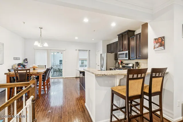 a kitchen with stainless steel appliances granite countertop a stove a refrigerator a kitchen island and chairs with wooden floor