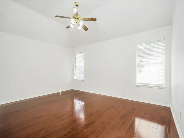 an empty room with wooden floor fan and windows