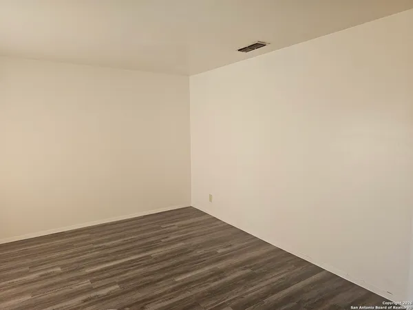 a view of an empty room with wooden floor and white wall