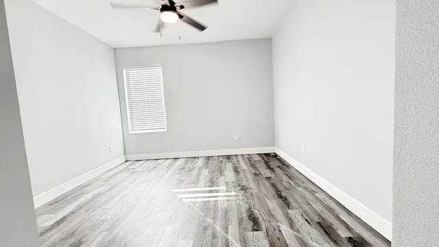 an empty room with wooden floor fan and windows