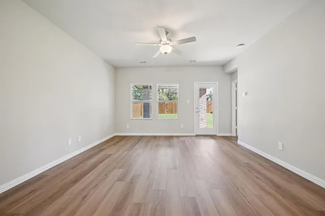 an empty room with wooden floor chandelier fan and windows